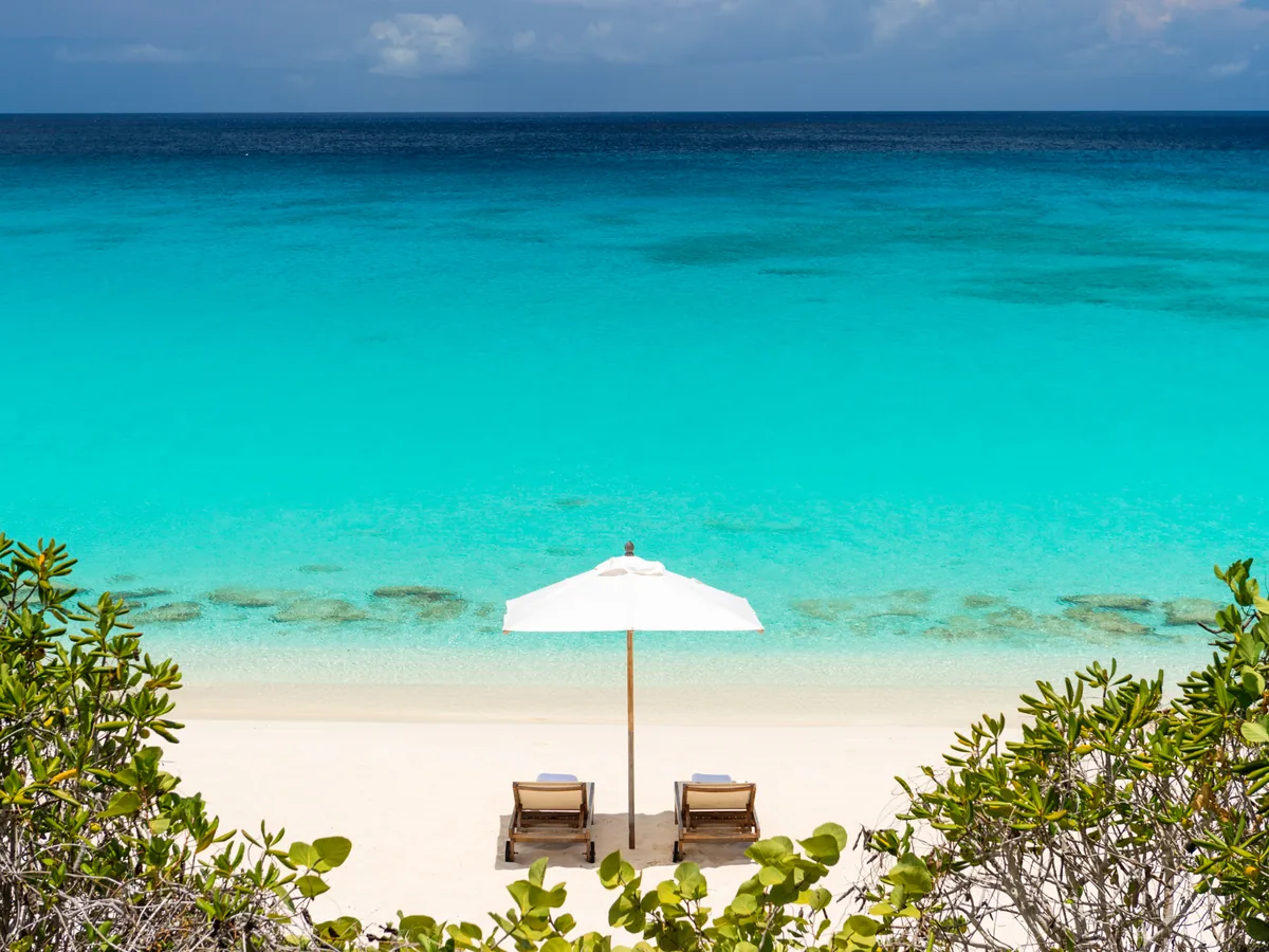 A quiet stretch of white-sand beach and turquoise water fronting a luxury villa resort