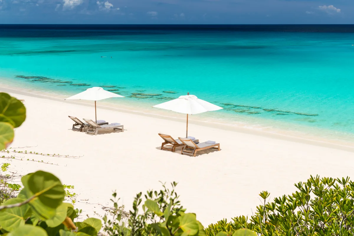 Two white umbrellas and loungers on a bright stretch of sand above clear turquoise sea