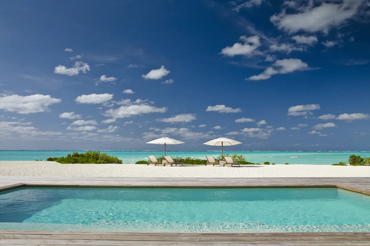 A quiet pool and sun umbrellas overlooking the turquoise sea at a beachfront hotel