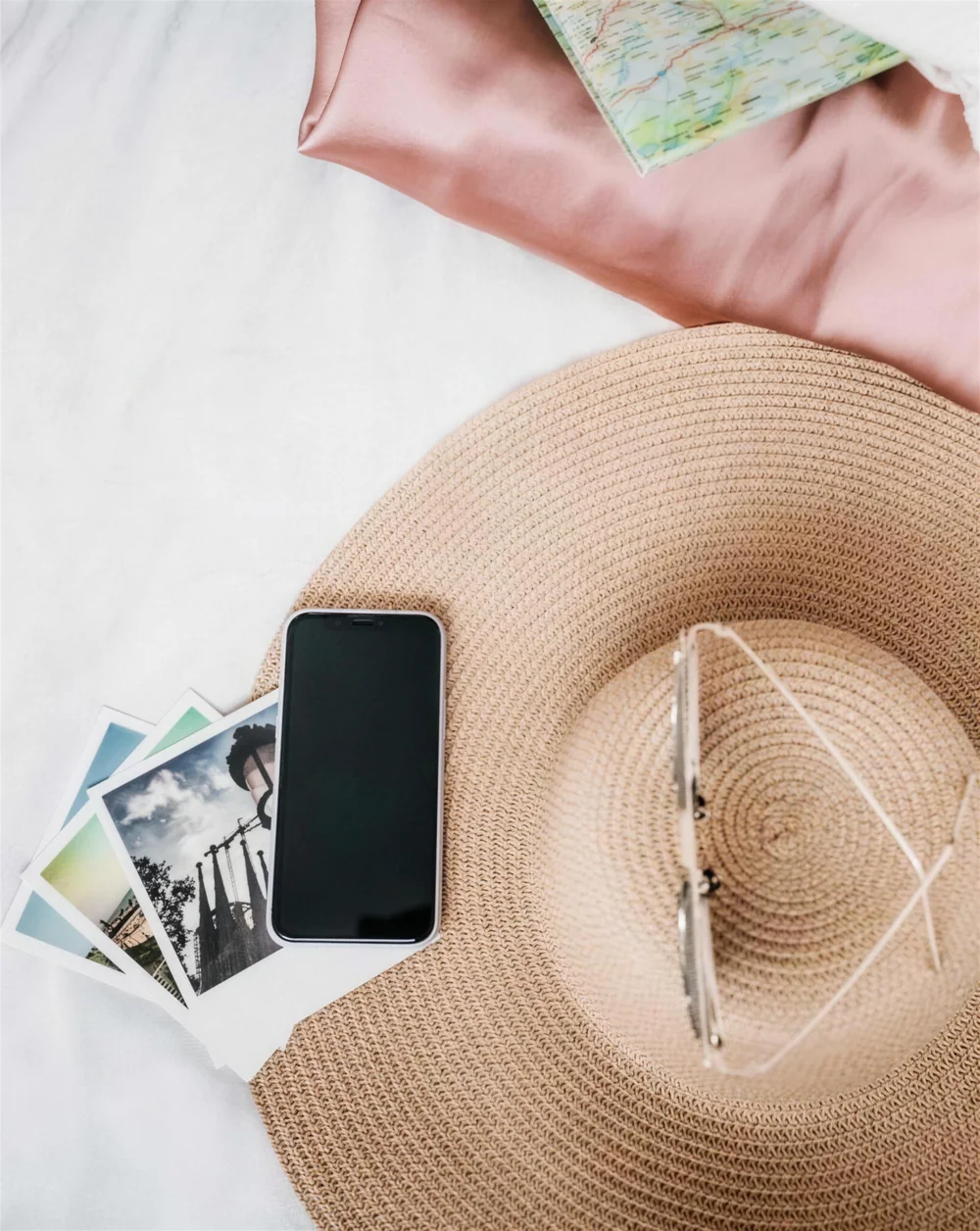 A sun hat, phone, map and travel photos laid out on crisp white linens