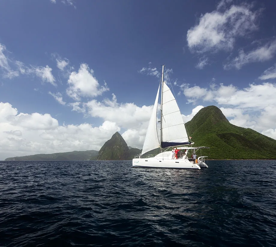 A catamaran under full sail off the Saint Lucia coast, the Pitons rising behind