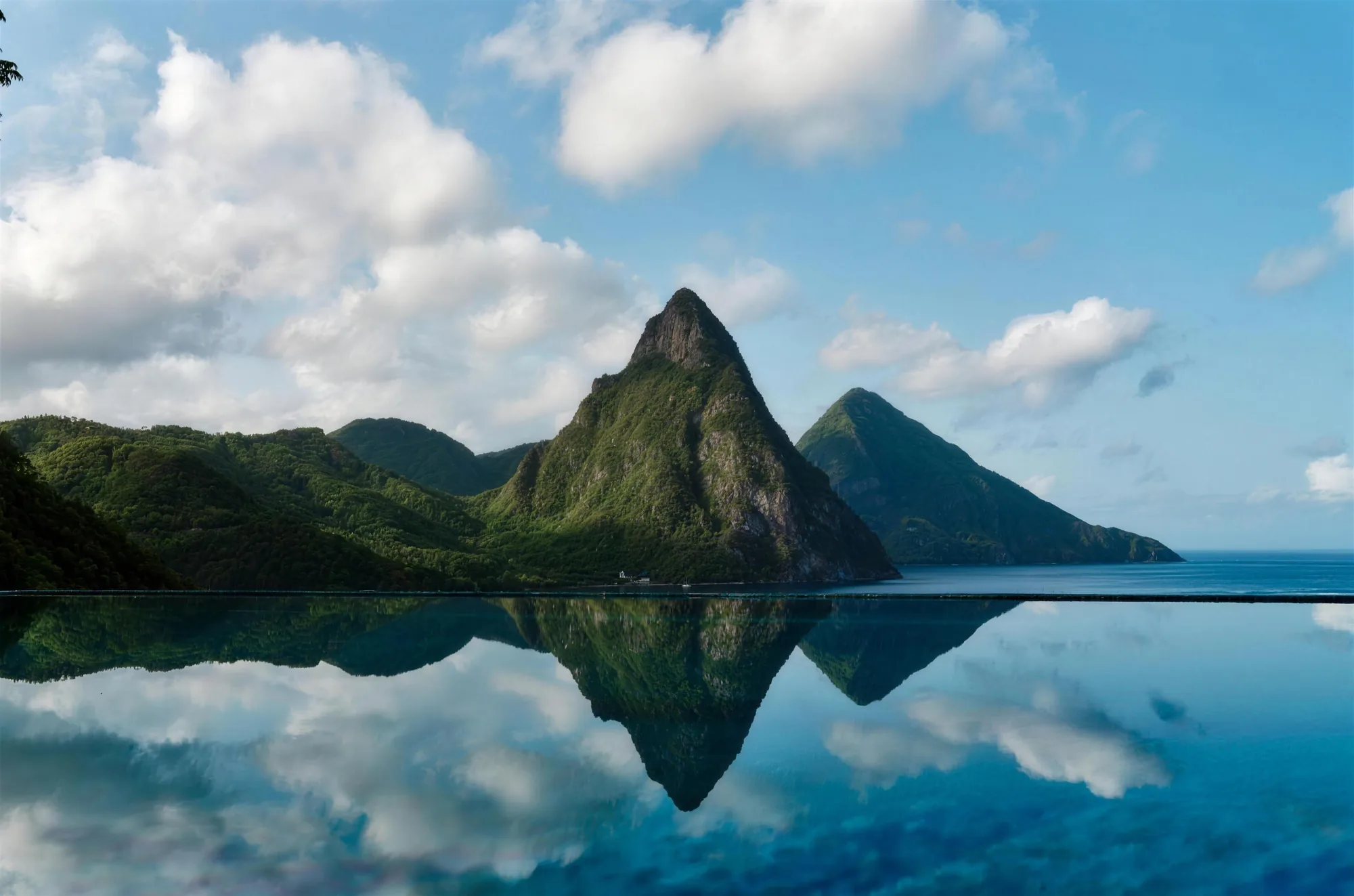 A still infinity pool reflecting the twin Pitons of Saint Lucia under a bright sky