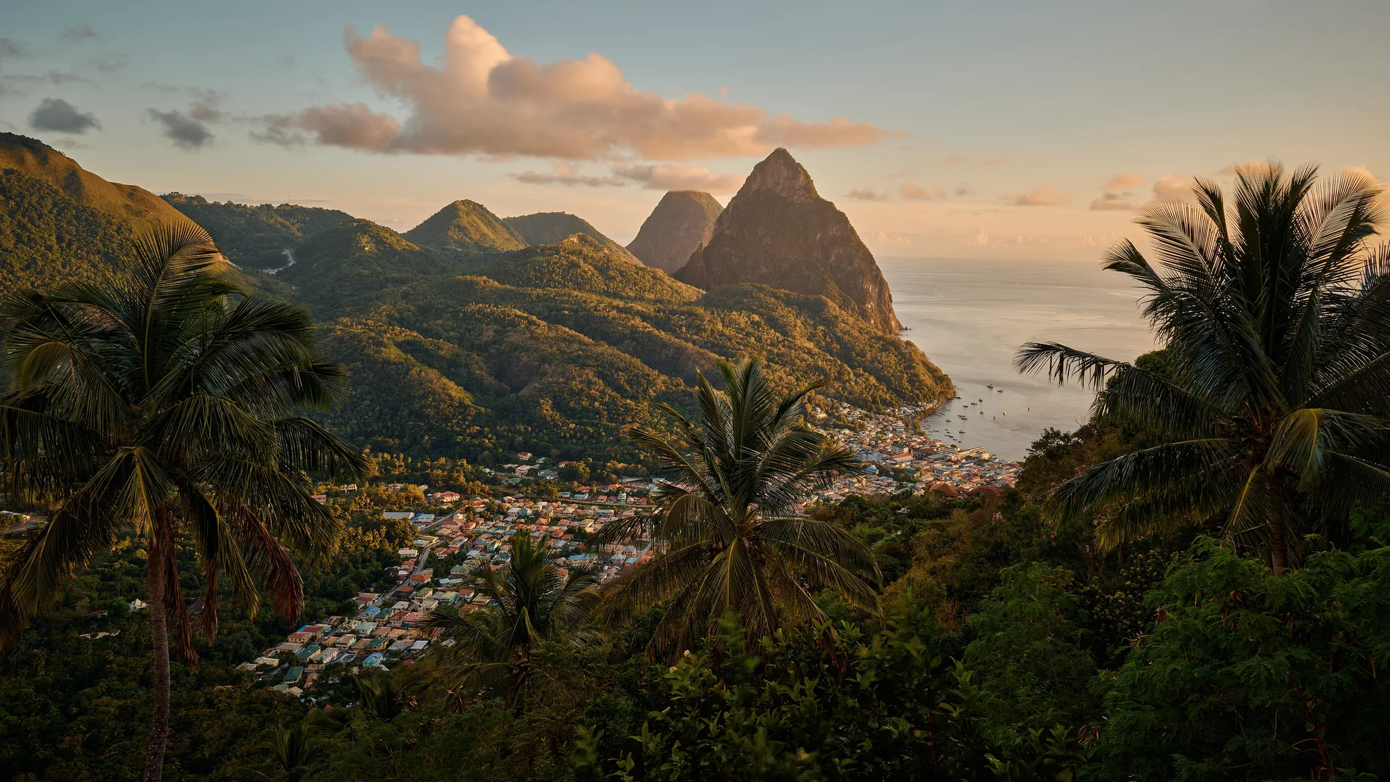 Golden-hour view over the palms and rooftops of Soufriere toward the twin Pitons of Saint Lucia