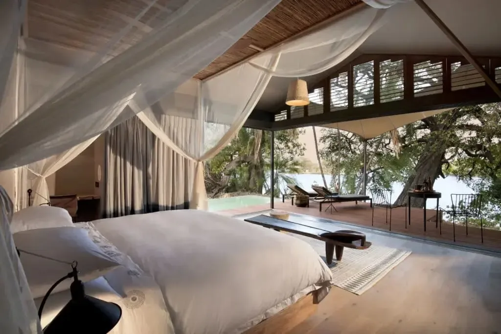 A canopied safari-lodge suite opening onto a private deck and plunge pool above a river
