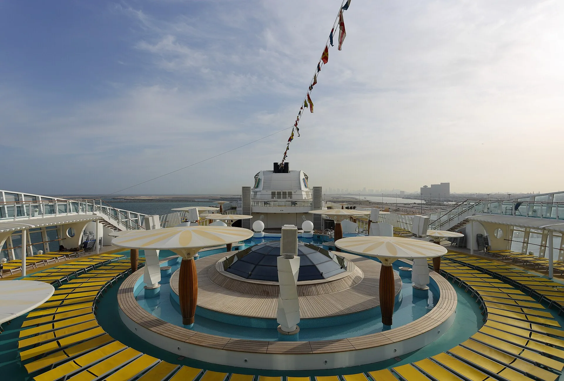 A calm cruise ship pool deck with loungers under a clear sky