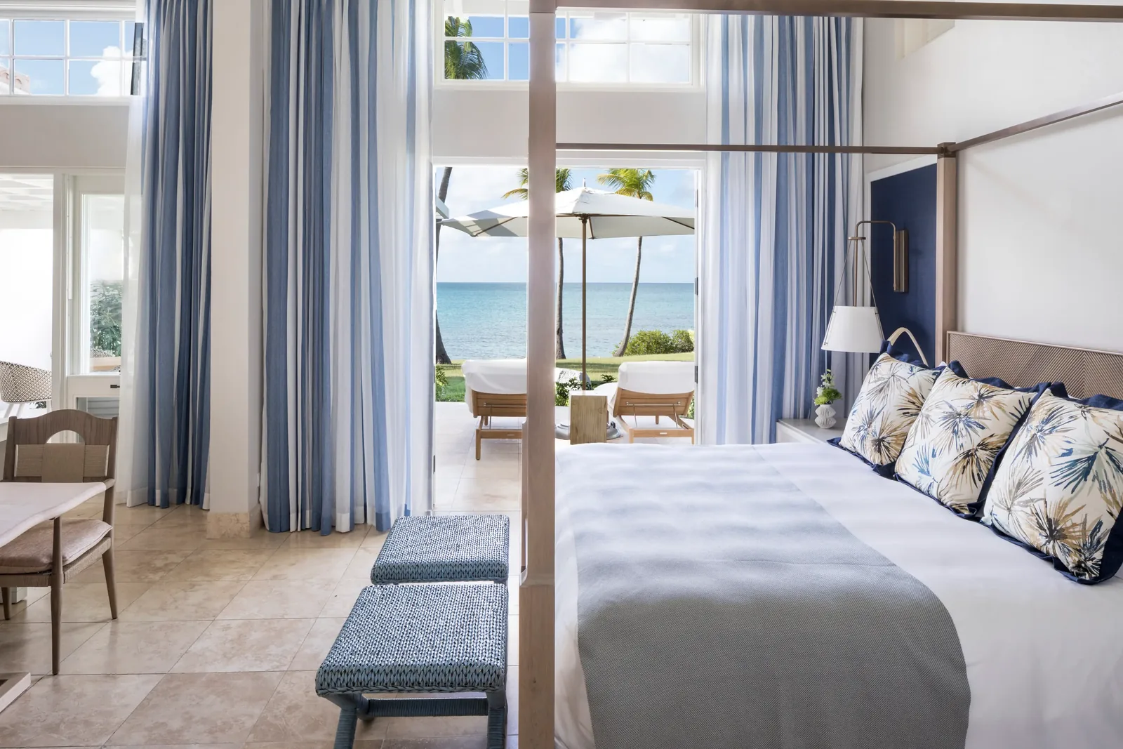A bright oceanfront suite with a four-poster bed opening to a beachfront terrace and turquoise sea
