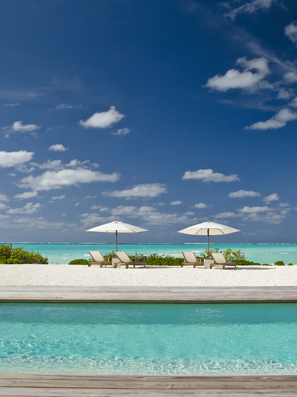 A bright pool and sun umbrellas above the turquoise sea at a beachfront villa